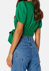 Top verde corto con maniche a sbuffo, annodato in vita. Abbinato a jeans in denim blu a vita alta con un classico design a 5 Tasche.