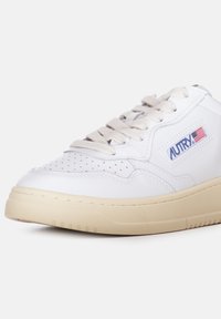 Sneaker in pelle bianca con suola in gomma crema, dettagli testurizzati, fori sulla punta e logo "AUTRY" con bandiera americana.