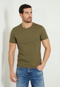 Oliven grøn kortærmet T-shirt lavet af glat bomuld, med et diskret "Guess" logo på brystet og en klassisk rund hals.