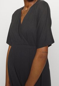 Czarna sukienka o odpowiednim kroju, z krótkimi rękawami, dekoltem w serek, marszczonym wcięciem w talii i miękkim materiałem. Posiada gładką fakturę i luźny krój.