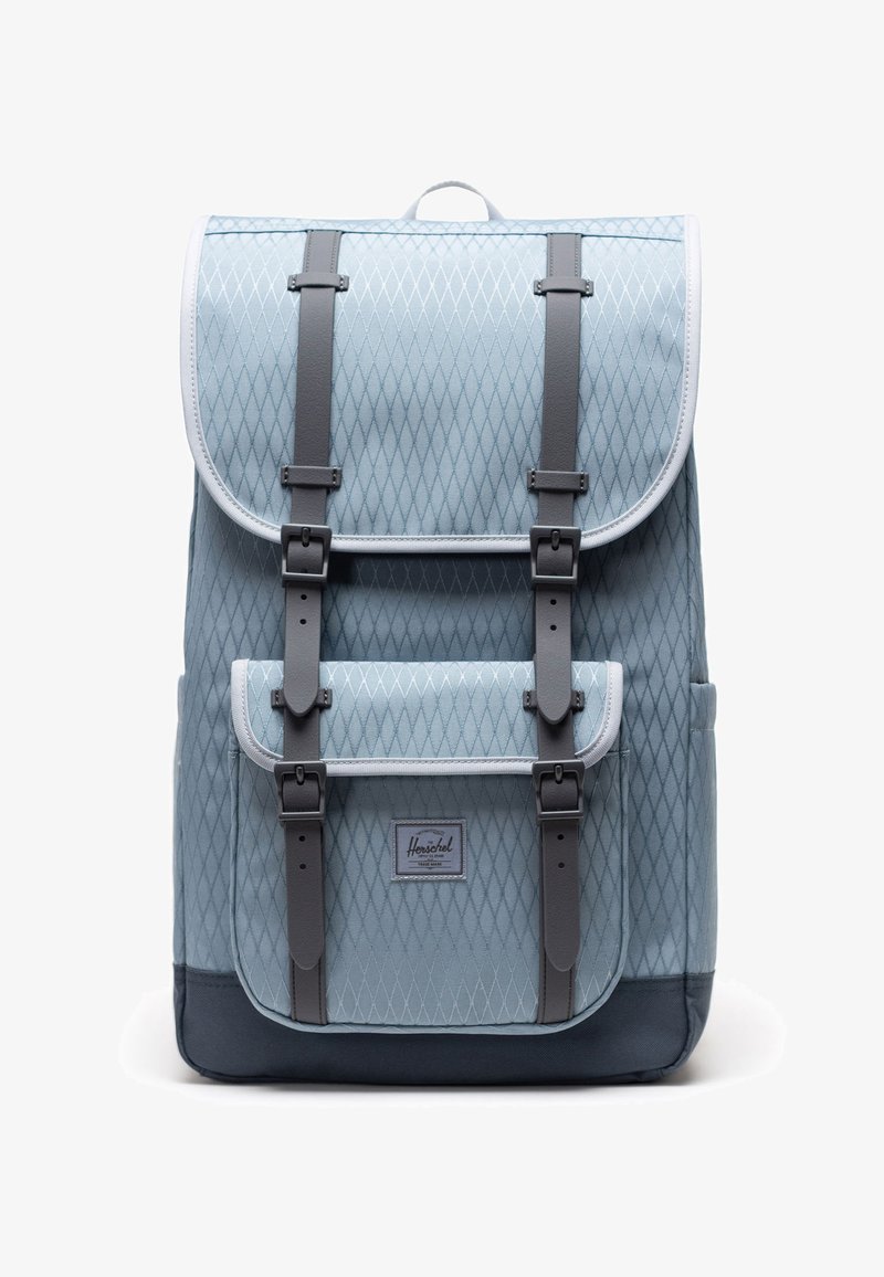 Sac à dos bleu clair avec motif en losanges, bretelles et boucles gris foncé, poche avant et panneau inférieur noir.
