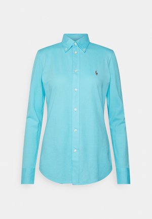 Camisa de manga larga azul claro con cuello abotonado, que presenta un pequeño logo de polo bordado en el pecho y cierre de botones en la parte delantera.