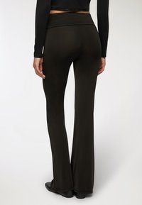 Pantaloni neri a zampa d'elefante con una texture morbida e una vita larga, che mostrano una finitura in tessuto liscia e una leggera lucentezza. Si indossano scarpe nere.