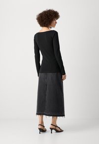 Top negro de manga larga con escote amplio, combinado con una falda maxi de denim oscuro con dobladillo deshilachado y sandalias de tacón negras.