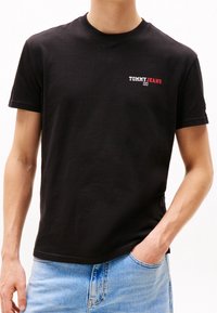 Czarna bawełniana koszulka z krótkim rękawem, z małym logo 'TOMMY JEANS' w kolorze czerwonym i białym po lewej stronie klatki piersiowej. Prosty okrągły dekolt.