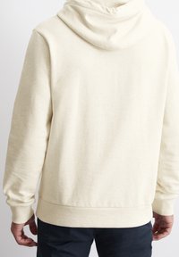 Felpa crema dal taglio rilassato, texture morbida, tasca a marsupio e polsini a coste. Presenta un cappuccio con cordino e un design semplice e pulito.