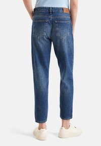 Modré džínové kalhoty s rovně střiženým designem, vybledlou texturou a výraznými zadními kapsami. Kombinovány s bílými teniskami pro ležérní vzhled.