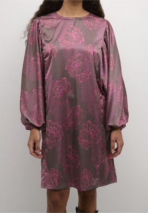 Donna che indossa un abito in raso al ginocchio con maniche lunghe e motivi floreali rosa su uno sfondo malva smorzato.