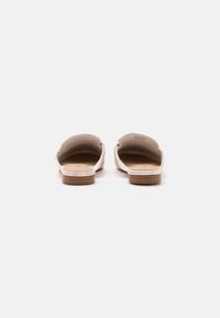 Un paio di mocassini rosa femminili, aperti sul retro, con tacco in legno basso, visti da dietro su uno sfondo bianco.