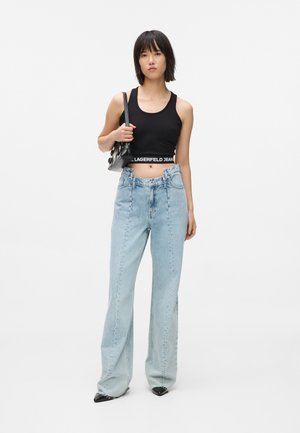 Black cropped tank top with white "LAGERFELD JEANS" logo, paired with light blue high-waisted wide-leg jeans and black pointed-toe heels.