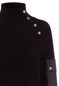 Schwarzer Strickpullover mit hohem Kragen, der silberne Druckknöpfe an der Schulter und einen strukturierten Stoff hat. Inklusive eines Lederakzents am Ärmel.