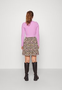 Un haut rose clair à manches longues associé à une jupe noire à motifs floraux. La jupe présente une taille froncée et un ourlet volé. Des bottes noires jusqu'aux genoux complètent le look.