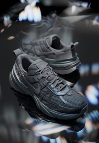 Chaussures de course Nike grises avec panneaux en mesh et synthétiques, lacées, placées sur une surface réfléchissante montrant leurs vues latérales et supérieures.
