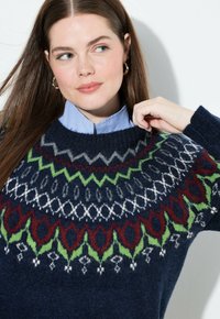 Maglione lavorato a maglia blu navy con un motivo Fair Isle multicolore in rosso, verde, grigio e bianco sulla parte superiore e sul colletto.