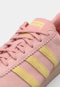 Roze nubuk tenisice s žutim tri pruge, s ravnim vezicama i valovitim rubom. Adidas logo na jeziku.