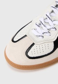 Sneaker with a combination of white leather and beige suede, black accents, perforated detailing, and textured rubber sole.