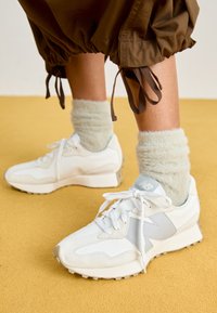 Zapatillas blancas y gris claro con paneles de ante y malla, que presentan una puntera redonda y suela de goma texturizada, acompañadas de calcetines esponjosos de color menta.