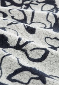 Strickstoff in Hellgrau mit großen dunkelblauen abstrakten Formen, der eine weiche Textur und einen leichten Glanz durch die Webart des Materials aufweist.