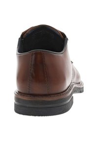 Chaussure en cuir marron avec un bout arrondi, des coutures visibles et une semelle en caoutchouc noir texturé. Présente un léger talon et une finition lisse.