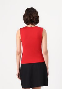 Top rojo sin mangas con un diseño ajustado, hecho de una tela suave, que presenta un escote redondo. Combinado con una falda negra.