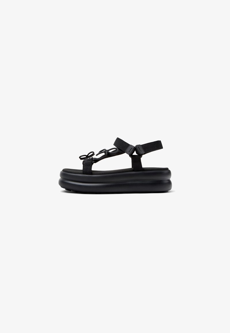 Sandal negru cu o talpă groasă din cauciuc, curele din material textil și catarame ajustabile. Prezintă accesorii decorative într-un design sub formă de buclă.