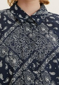 Navyblaues Hemd mit Knöpfen, mit weißen, aufwendigen Paisley- und Blumenmustern, ausgestattet mit einem spitzen Kragen.