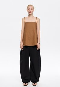 Top marrone senza maniche con scollatura quadrata, realizzato in tessuto testurizzato. Abbinato a pantaloni neri larghi. Design semplice, dettagli minimi.