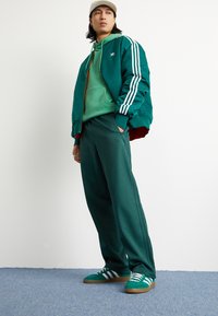 Vihreä pommikaveri takki valkoisilla raidoilla, siihen sopiva vihreä huppari ja löysät vihreät collegehousut. Vihreät urheilukengät valkoisilla raidoilla.