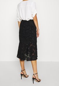Svart blommig spetsmidikjol med genomskinlig overlay och scalloped nederkant. Kombineras med en lös vit blus och svarta strap high heels.