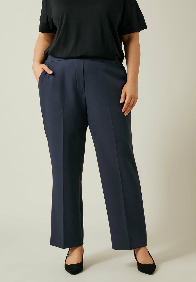 Navyblauwe wijde broek met een soepele textuur, zijzakken en een getailleerde pasvorm. Gepaard met een losse zwarte top en zwarte hakken.