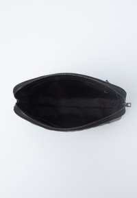 Borsa a zip nera con un'esterno testurizzato, foderata con un tessuto nero liscio. Si apre ampiamente per un facile accesso allo spazio interno di stoccaggio.