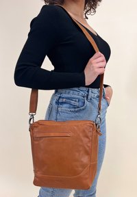 Borsa a tracolla in pelle tannata con forma piatta, tracolla regolabile e tasca frontale. Presenta una texture liscia e una branding discreta.