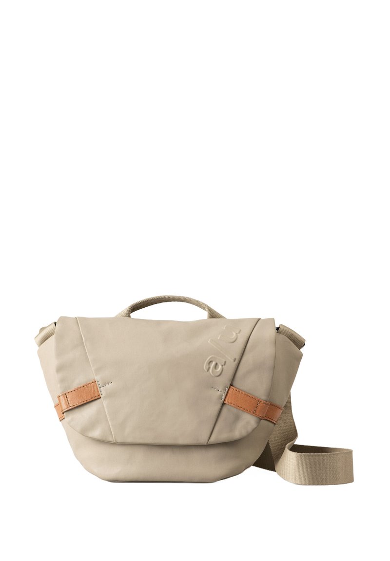 Beige Schultertasche mit strukturiertem Oberflächenmaterial, ausgestattet mit einem oberen Griff, verstellbarem Riemen und einem braunen Lederakzent an der Klappe.