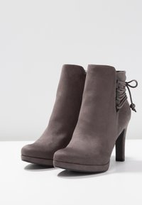 Stivali alla caviglia in suede grigio con tacco alto, punta rotonda e dettagli con lacci sul lato. Texture liscia con un design pulito e minimale.
