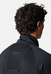 Zwarte sportpullover met hoge kraag, textuurstof, hexagonaal patroon en een iets verhoogd logo op de rug.