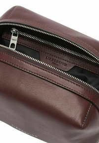 Bordowa skórzana torba z zamkiem u góry, wyposażona w srebrne okucia, gładką fakturę i wytłaczane logo z przodu.