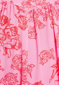 Tissu rose présentant un motif répétitif de chérubins rouges et de dessins floraux ornés, avec des plis sur la partie supérieure.