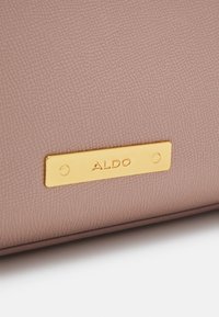 Roze leren tas met textuur, voorzien van een gouden metalen ALDO-logo plaat. Het oppervlak heeft een gebobbeld patroon, wat visuele interessen en detail toevoegt.