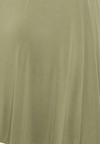 Top verde oliva feito de um tecido suave e leve. Apresenta um corte solto com uma textura suave e um brilho sutil, exibindo um drapeado suave.