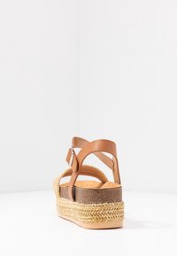 Brun läderklack med en plattform i jute-stil, justerbart ankelband och rund tå. Texturerad sula för grepp.