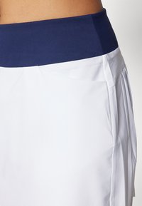 White skirt with a navy waistband, featuring pleated design and smooth texture. Focus on comfort and functionality in active wear.