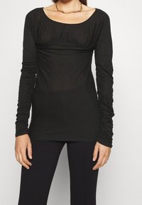 Zwarte top met lange mouwen, gemaakt van een lichtgewicht, doorschijnende stof. Heeft een ronde halslijn en geplooide details bij de buste en mouwen.