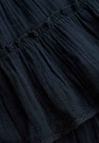 Tissu bleu marine foncé à texture froncée et plissée avec un détail subtil de bordure en dentelle sur un textile superposé.
