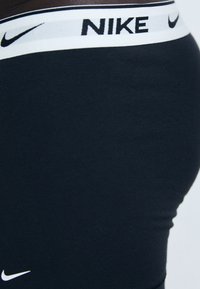 Schwarze Nike Leggings mit einem breiten elastischen Bund und kontrastierendem weißem Logo. Glatte Textur und figurbetontes Design, das für Komfort sorgt.