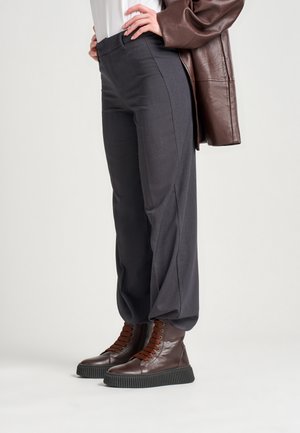 Pantalones grises ajustados con una textura suave y un corte recto, combinados con botas altas marrones que tienen suelas texturizadas y un diseño de cordones.