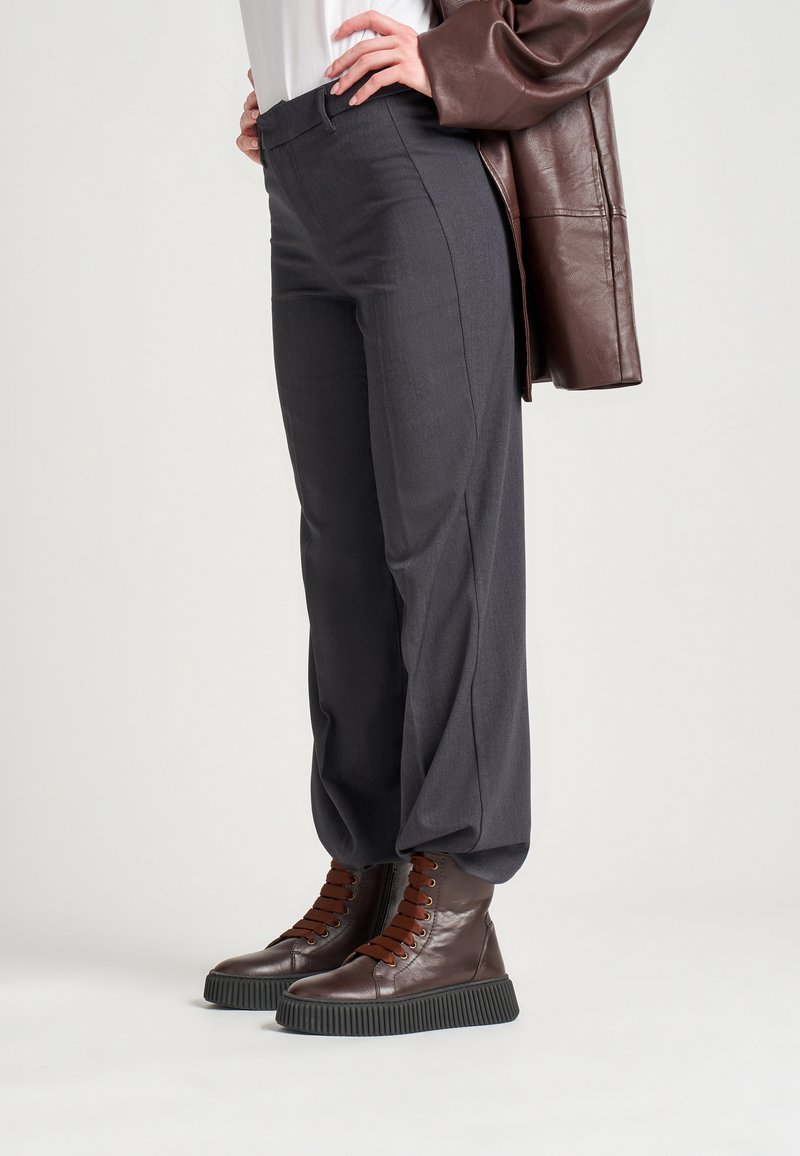 Pantalones grises ajustados con una textura suave y un corte recto, combinados con botas altas marrones que tienen suelas texturizadas y un diseño de cordones.