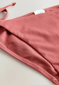 Roze bikini-top met een gladde, textuurachtige afwerking, met een eenvoudig ontwerp en verstelbare touwtjes aan één kant.