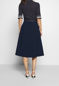 Navy blue cotton skirt, knee-length, with a gathered waistband and smooth texture. Worn with white high-heeled shoes, minimal detailing.