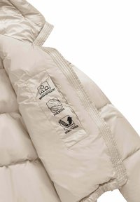 Beige gewatteerde jas mouw met geprinte iconen die waterafstotend, echte dons vulling en windstopper kenmerken aangeven.