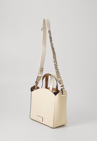 Beige gestructureerde handtas met korte handvatten en een verstelbare lange schouderband met de tekst "KARL LAGERFELD", weergegeven op een effen lichte achtergrond.